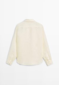 Crèmekleurig overhemd met lange mouwen, klassieke kraag, knoopmanchetten en een rechte zoom, van achteren getoond op een witte achtergrond.