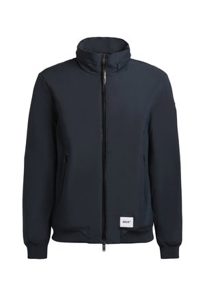 Tumedast sinine bomber-jakk kõrge kaelusega, lukuga kinnitamine, kaks küljetaskut, soonikkoes varrukad ja kangast embleem alläärtes. Sile materjal.