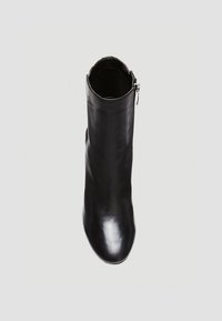 Botín de cuero negro hasta el tobillo con una textura suave, punta afilada y detalle de cremallera plateada en el lateral. Diseño minimalista, sin patrones visibles.