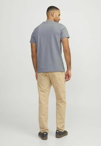 Tricou gri cu m�ânecă scurtă și pantaloni bej deschis. Tricoul are un guler rotund; pantalonii au buzunare la spate și sunt purtați cu adidași negri.