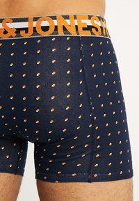 Boxer in blu navy con un motivo a pois arancioni e bianchi; l'elastico in vita riporta la scritta "JONES" in caratteri arancioni.