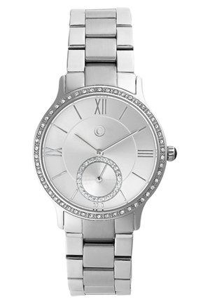 Montre en métal argenté avec un cadran rond, des chiffres romains et un petit sous-cadran. La lunette est ornée d'un anneau de strass. Style de bracelet en métal.