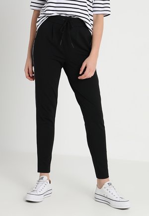 Sorte joggerbukser med snor i taljen, med hvide sidelægger og en tætsiddende pasform. Kombineret med hvide sneakers for et afslappet look.