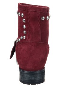 Bottine en daim rouge avec des accents de clous argentés le long du côté. Semelle plate noire avec un talon légèrement surélevé. Dotée d'un détail de boucle latérale.
