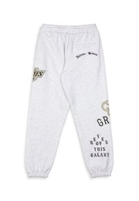 Pantalon de survêtement gris avec taille élastique et poignets, comportant des textes et logos imprimés en noir et en or dans différentes polices. Texture de tissu douce.