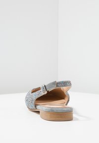 Sandalo grigio in suede con cinturino alla caviglia, adornato con decorazioni argento e blu, dotato di una suola piatta in legno e design con tacco aperto.
