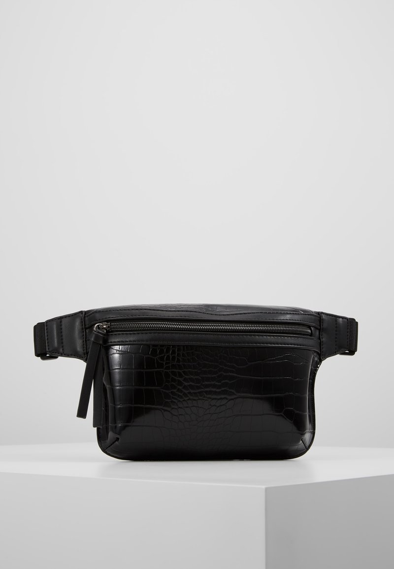 Sac banane en simili-cuir effet crocodile noir avec poche avant zippée et sangle ajustable, exposé sur un socle blanc sur fond gris.