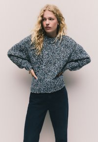 Suéter de punto en tonos azul oscuro y gris claro, con un corte relajado, puños y dobladillo acanalados, y un patrón texturizado y grueso.