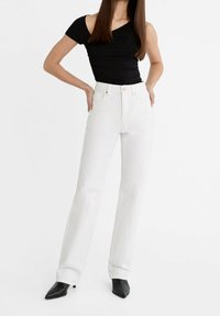 Jeans bianchi a gamba dritta in denim, caratterizzati da un alto vita, chiusura con bottone e dettagli di cucitura sottili. Abbinati a un top aderente nero.