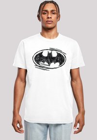 Hvit bomulls t-skjorte med et svart skisseaktig Batman-logo sentrert på brystet, korte ermer og standard rund hals.
