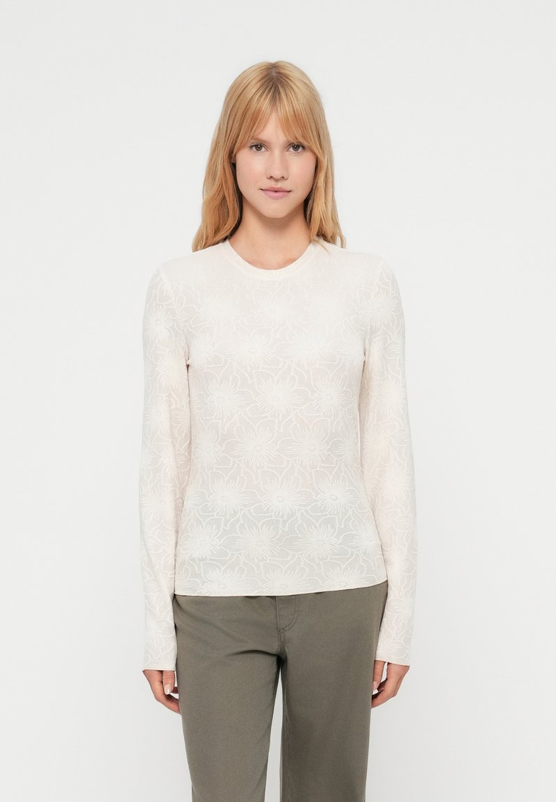 Μακρυμάνικο εφαρμοστό τοπ σε ανοιχτό μπεζ χρώμα με φλοράλ δαντέλα, στρογγυλή λαιμόκοψη, λεία υφή, συνδυασμένο με πράσινο παντελόνι.