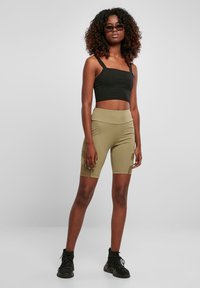 Débardeur court noir, short de cycliste vert olive avec poches latérales, texture lisse, coupe ajustée. Mannequin portant des baskets montantes noires.