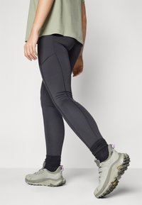 Högmidjade svarta leggings med en slät textur och sömdetaljer, i kombination med ljusgrå löparskor och mörka strumpor.