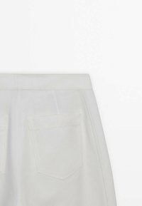 Pantalon blanc avec poches arrière visibles et coutures apparentes, présenté de la taille jusqu'à mi-cuisse sur un fond blanc uni.