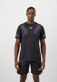 Sort atletisk t-shirt med korte ærmer, teksturerede detaljer og letvægtsstof, parret med matchende shorts. Har et logo på brystet og kanten.