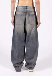 Φαρδιά μπλε τζιν με ξεθωριασμένο φινίρισμα, δύο πίσω τσέπες και ελαφριά φθορά στο τελείωμα, με άνετη εφαρμογή και ψηλή μέση.