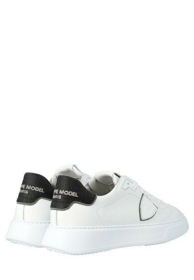 Sneaker bianche basse con tacco nero e logo in rilievo sul lato, progettate per un uso casual, con lacci e suole imbottite.
