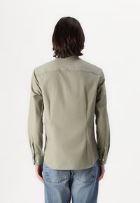Olive green button-up shirt with a straight cut, long sleeves, and side slits. Features a plain texture and minimalistic design.