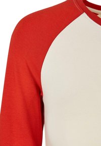 Kurzärmliges Shirt mit rotem Raglan-Design, featuring einen weichen weißen Körper und glatter Textur. Keine Muster oder Hardwaredetails sichtbar.