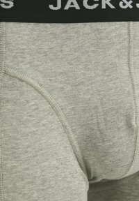 Harmaat boxerit, jotka on valmistettu pehmeästä kankaasta, mustalla elastisella vyötärönauhalla, jossa lukee "JACK & J" valkoisella kirjaimilla, sekä litteillä saumoilla.