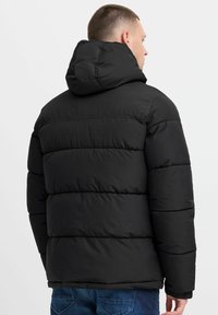 Black puffer jacket with a hood, featuring quilted panels, elastic cuffs, and a smooth texture. Minimal design with no visible logos.