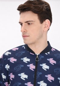 Giacca bomber navy con chiusura a zip, caratterizzata da un motivo di tartarughe blu e rosa. Tessuto morbido con colletto e polsini a costine.