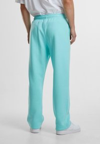 Light turquoise sweatpants with an elastic waistband, side pockets, and a relaxed fit, paired with white sneakers.