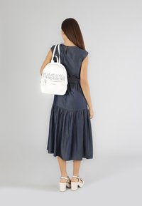 Sininen farkkuinen mekko, jossa on laajahelma, yhdistettynä valkoiseen reppuun, jossa on laserleikattu kukkakuvio ja vetoketjullinen tasku. Valkoiset platform-sandaalit.