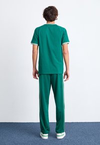 Grön, kortärmad t-shirt med kontrasterande grön kant, matchad med gröna byxor som har sidostråk och en avslappnad passform.