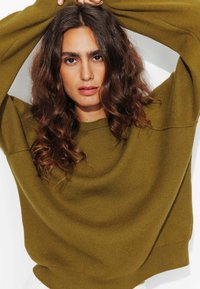 Pull en maille vert olive avec des manches larges et amples et un col rond. Texture douce avec un léger côtelé aux poignets et à l'ourlet.