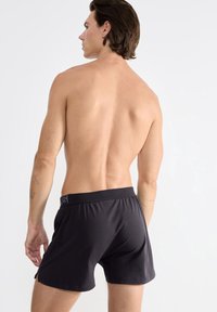 Černé bavlněné boxerky s elastickým pasem, s malým logem. Model se otáčí zády, ukazuje zadní pohled.