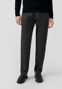 Szare spodnie w kratę o prostym kroju i subtelnej fakturze, zestawione z czarnymi mokasynami, noszone z czarnym swetrem.