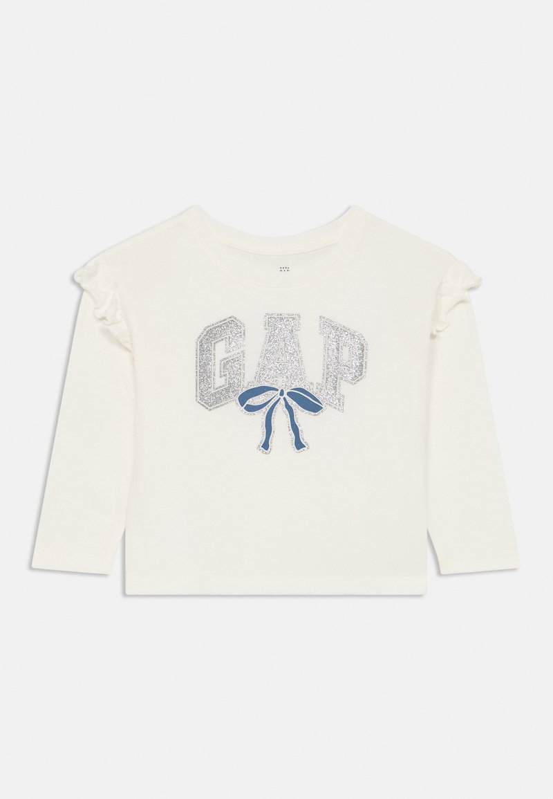 Maglietta bianca a maniche lunghe con un logo "GAP" glitterato e un design a fiocco blu. Delicati accenti arruffati sulle spalle. Materiale in cotone morbido.