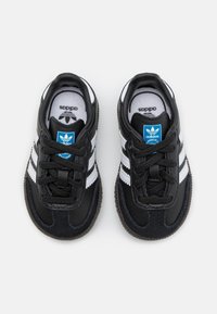 Schwarz-weiße Sportschuhe mit einem strukturierten Lederoberteil, drei weißen Streifen, runden Schnürsenkeln und einem blauen Logotag auf der Zunge.