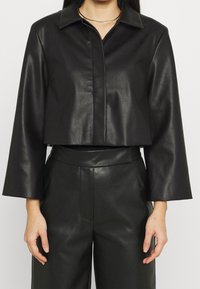 Giacca in pelle nera corta con colletto, maniche lunghe e una texture liscia, abbinata a pantaloni in pelle a vita alta dello stesso colore.