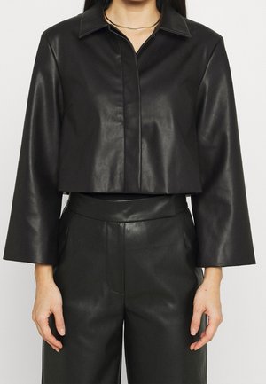 Chaqueta de cuero negro corta con cuello, mangas largas y una textura suave, combinada con pantalones de cuero de talle alto a juego.