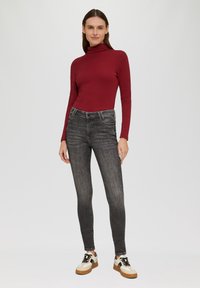 Rode coltrui, grijze skinny jeans met voorzakken en crèmekleurige sneakers met zwarte veters en een bruine rubberen zool.