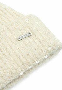 Kremowa dziana czapka z prążkowanym wzorem, ozdobiona małymi białymi cekinami, posiada srebrny metkę z nazwą marki.