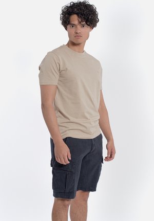 Beige t-shirt met korte mouwen, gecombineerd met donkere cargoshorts. T-shirt gemaakt van gladde stof; shorts hebben zijzakken en een relaxte pasvorm.