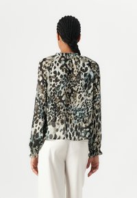 Průsvitná blůza v černé a béžové barvě s leopardím potiskem, dlouhými rukávy se šňůrkovými manžetami a kulatým výstřihem.