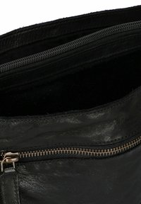 Ingrandimento di una sezione di borsa in pelle nera che mostra due scomparti con cerniera, uno parzialmente aperto, rivelando la fodera interna scura.