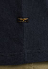 Tela de camiseta de rayas en azul marino con una etiqueta cosida que presenta un logotipo dorado que dice "AMERICAN CLASSIC".