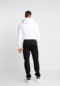 Zwarte cargobroek met zijzakken, elastische tailleband en taps toelopende boorden, gecombineerd met een witte hoodie met een trekkoord en geribde boorden.