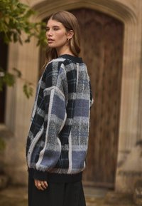 Pull en tartan surdimensionné dans des tons marine, gris et blanc. Tissu texturé avec des poignets et un ourlet côtelés. Coupe décontractée, avec des épaules tombantes.