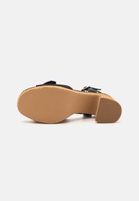 Sorte sandaler med en vevd jute hæl, gummisåle og justerbare reimer. Teksturert underside, formet fotbed for komfort.
