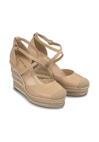 Espadrillas a zeppa beige con cinturini incrociati, suola in gomma e tacco in juta intrecciata. Caratterizzate da un cappuccio frontale intrecciato e dettagli metallici sulla suola.