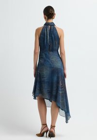 Vestido de tirantes en tejido transparente azul oscuro con un dobladillo asimétrico, que presenta un sutil patrón de paisley y un detalle de abertura en la espalda.