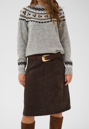 Woman wearing a gray patterned knit sweater, brown corduroy skirt, wide brown belt with gold buckle, and brown suede boots.