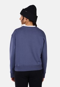 Sweter w kolorze stonowanego niebieskiego, z okrągłym dekoltem i ściągaczami. W zestawieniu z fakturowaną czarną czapką.