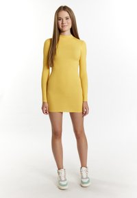 Abito giallo a costine con maniche lunghe e collo alto, abbinato a sneakers multicolori alte. Texture liscia.